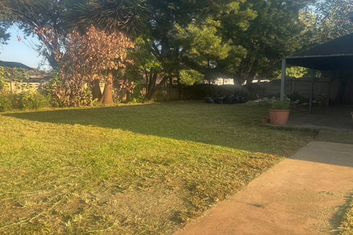 A spacious rear garden featuring a large lawn area, mature trees, and a covered patio space, providing a private outdoor setting.