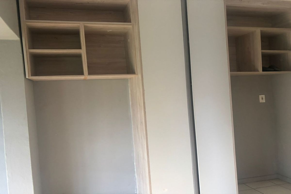 A bedroom interior featuring built-in wooden shelving units and cabinetry, providing ample storage space with a neutral wall finish.