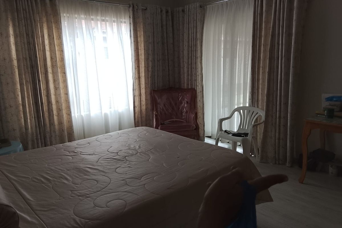 A bedroom featuring neutral wall tones, large windows with floor-to-ceiling curtains, and light-colored flooring.