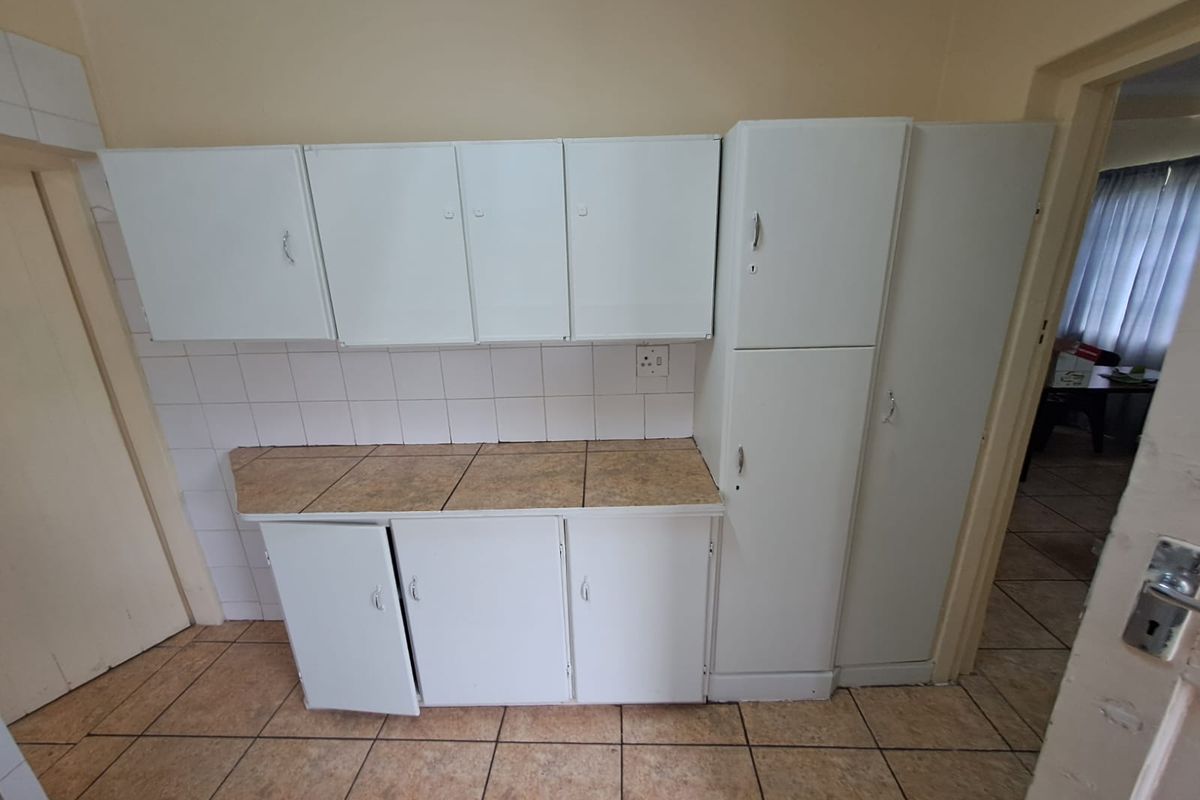 A functional kitchen area featuring white cabinetry, tiled backsplash, and tiled flooring, offering a practical layout for food preparation and storage.