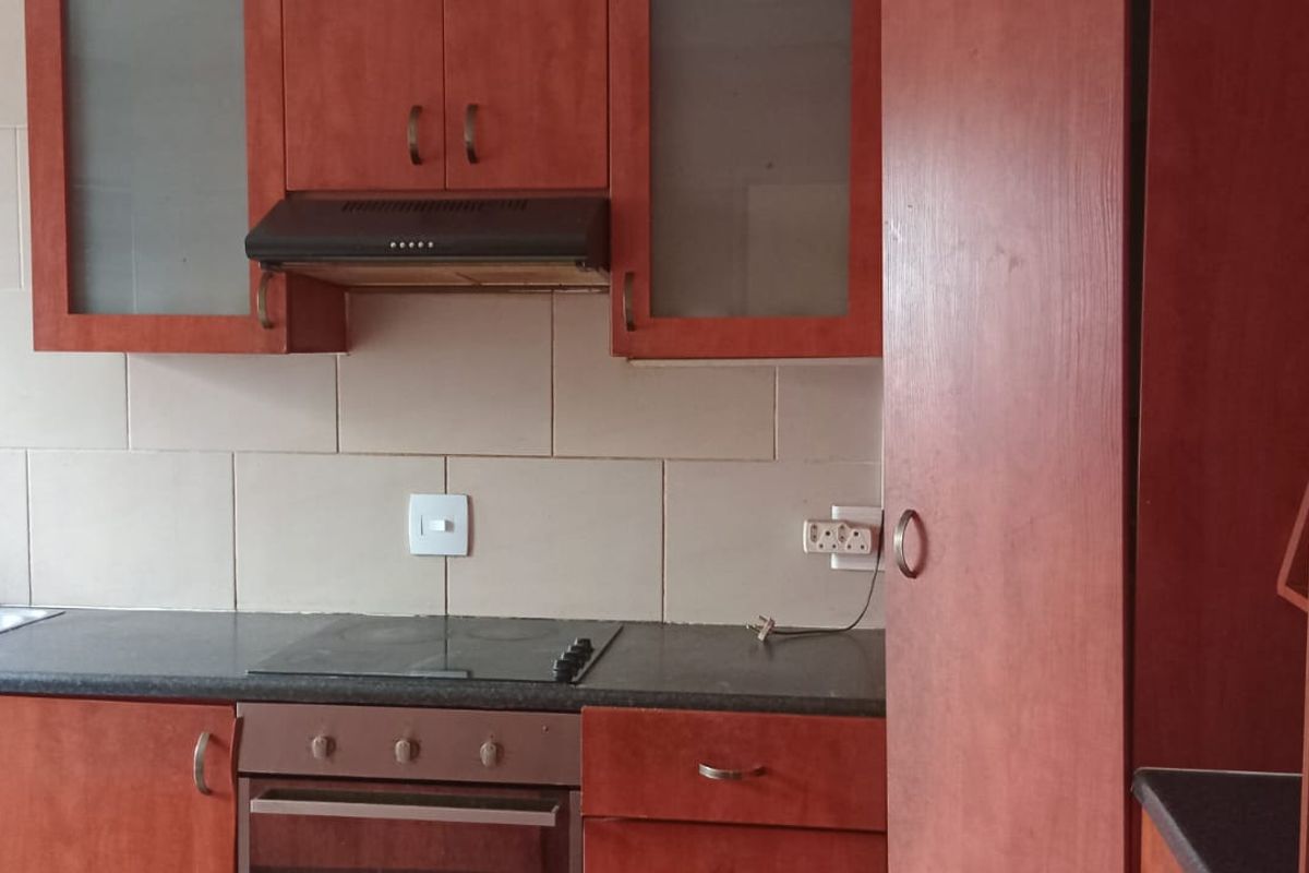 A functional kitchen featuring wood-look cabinetry, a built-in oven with hob, extractor fan, and tiled backsplash.