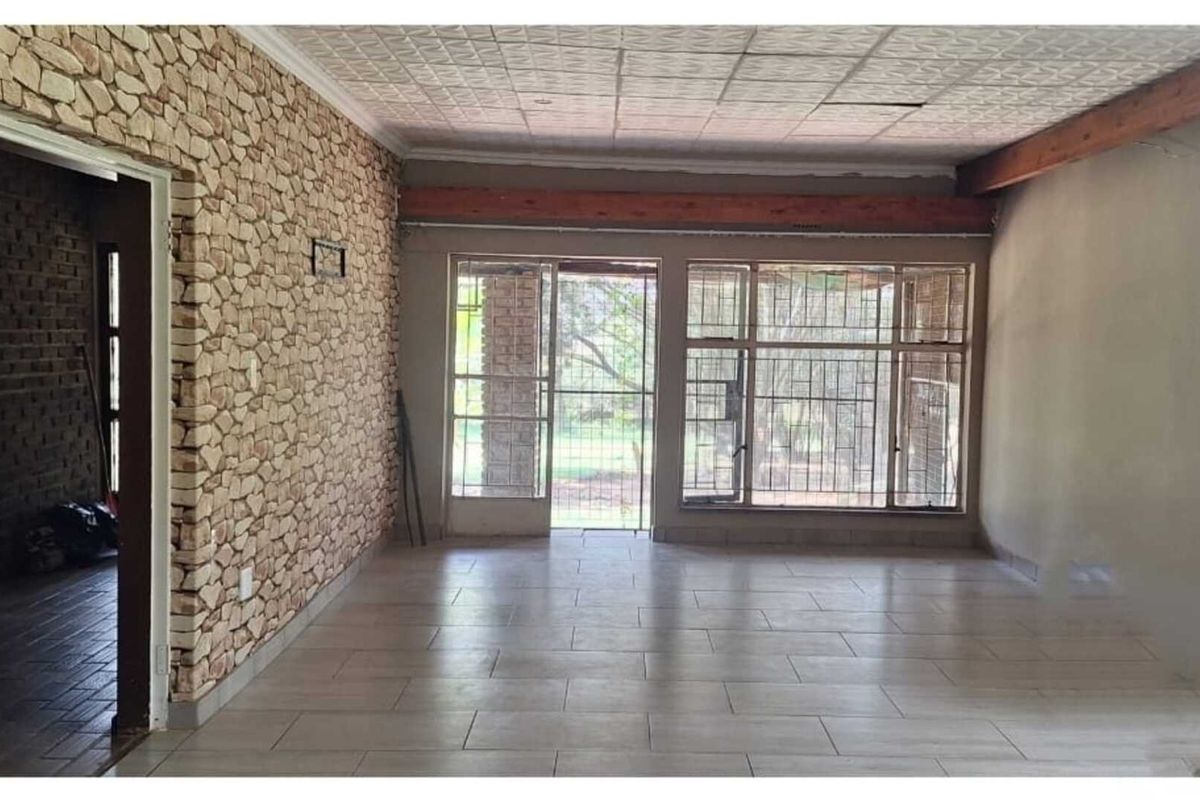 Spacious living area featuring stone-clad feature wall, tiled flooring, and large windows with security bars, offering potential for renovation.