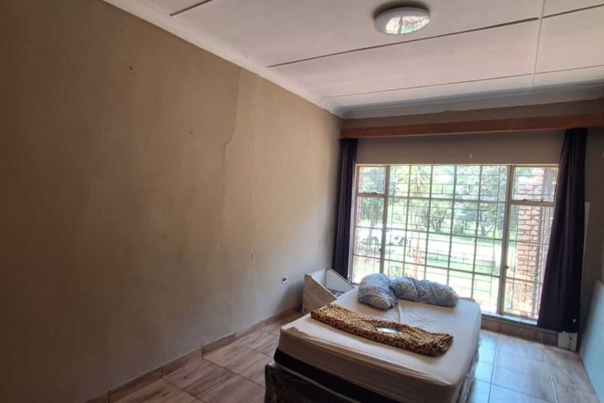 A bedroom featuring tiled flooring and a large window with security bars, offering natural light and views of the surrounding property.