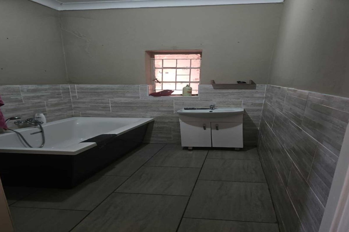 A functional bathroom featuring a built-in bathtub, a vanity cabinet with a basin, and tiled wall and floor finishes.