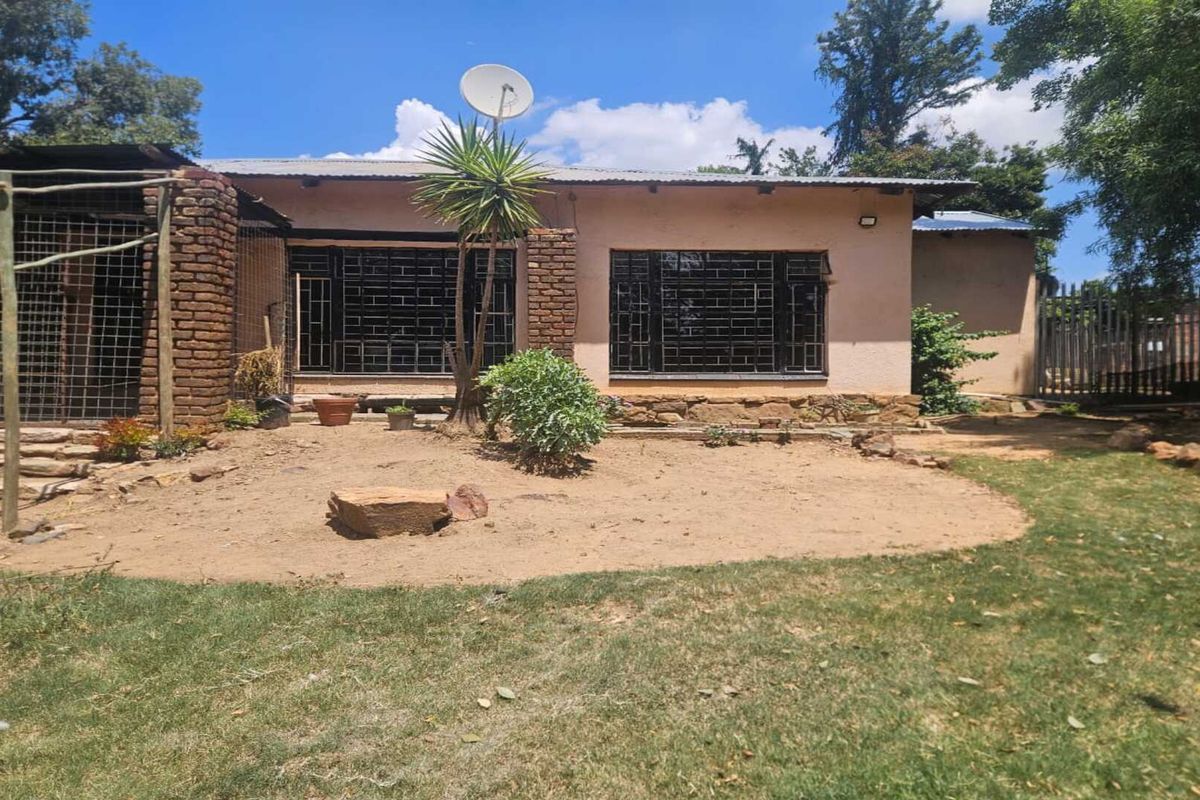 Rear view of a small holding dwelling featuring brick and plaster construction, metal security bars on windows, and a satellite dish.