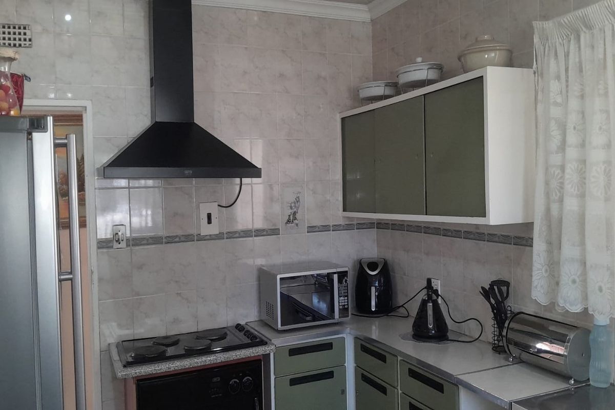 A functional kitchen featuring built-in cabinetry, a black extractor fan, and a stove, finished with tiled walls and countertops.
