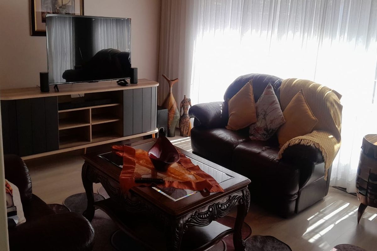A comfortable living room featuring light-toned laminate flooring and large windows with sheer curtains, providing ample natural light.