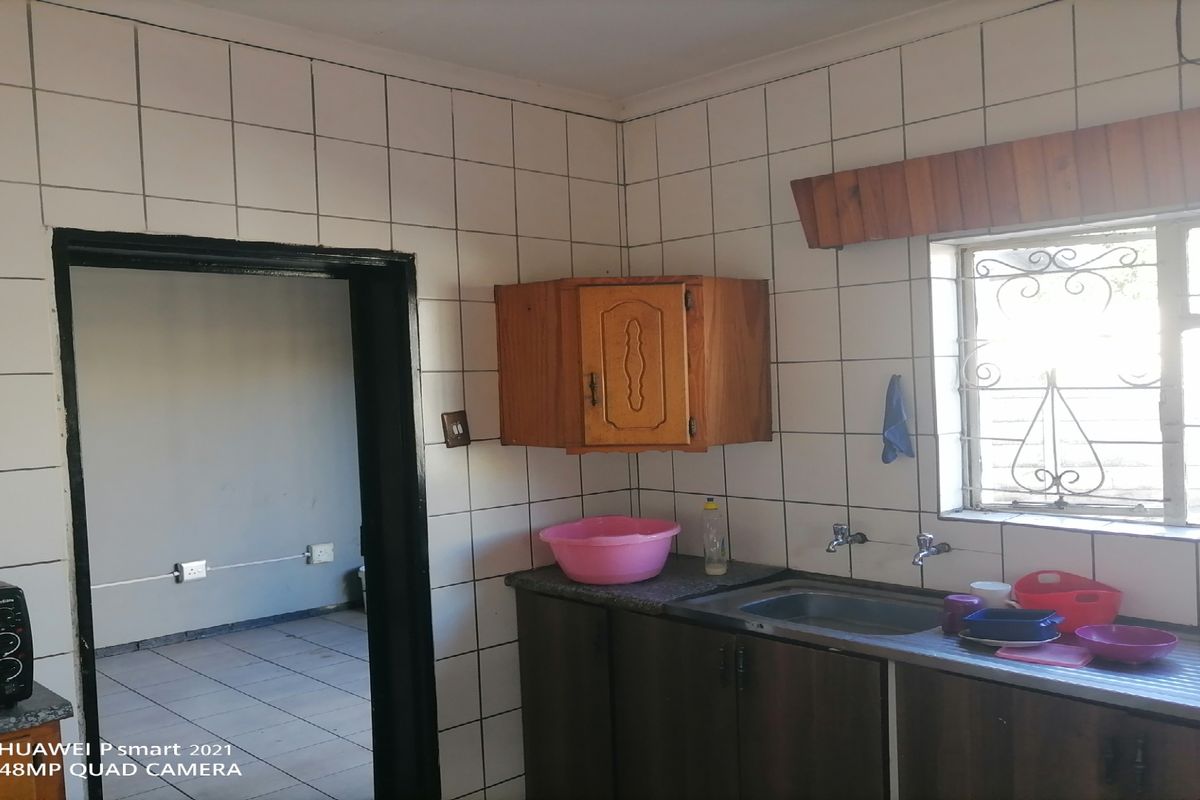 A functional kitchen area featuring tiled walls, built-in wooden cabinetry, a stainless steel sink, and a window with security bars.