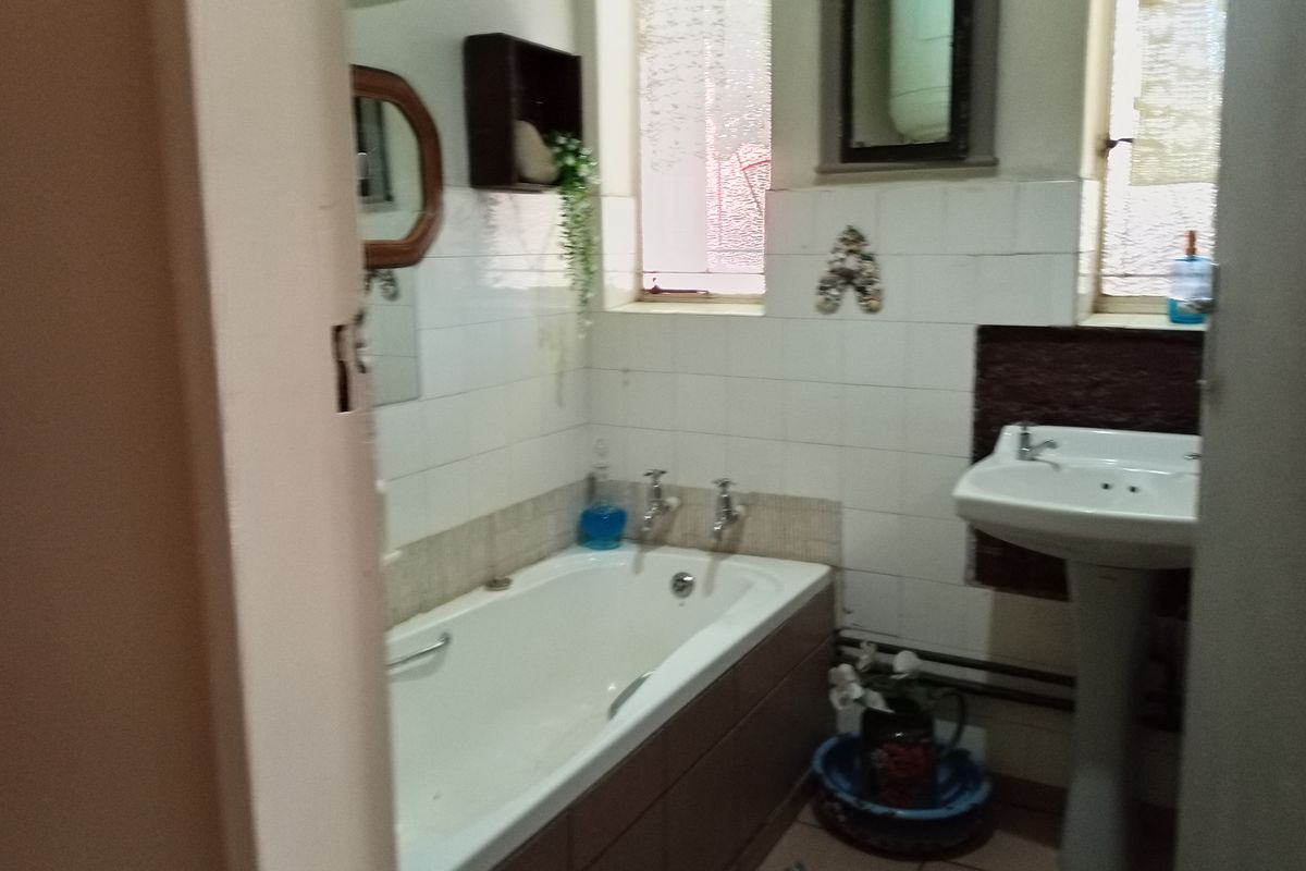 A dated bathroom featuring a built-in bathtub, pedestal basin, and tiled wall finishes, offering potential for modernization and renovation.
