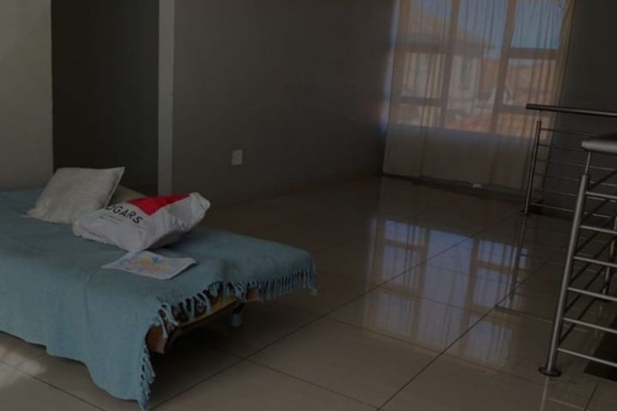 A spacious living area featuring large format floor tiles, neutral wall finishes, and a metal staircase railing.