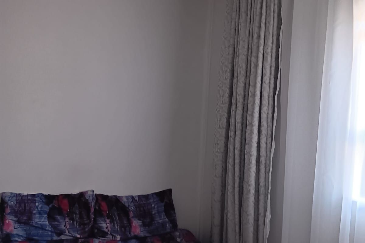 A bedroom featuring neutral wall finishes and floor-to-ceiling curtains, providing a simple and functional living space.