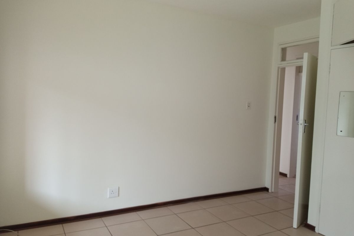 A bright, empty bedroom featuring neutral tiled flooring, built-in cupboards, and a doorway leading to an adjacent space.
