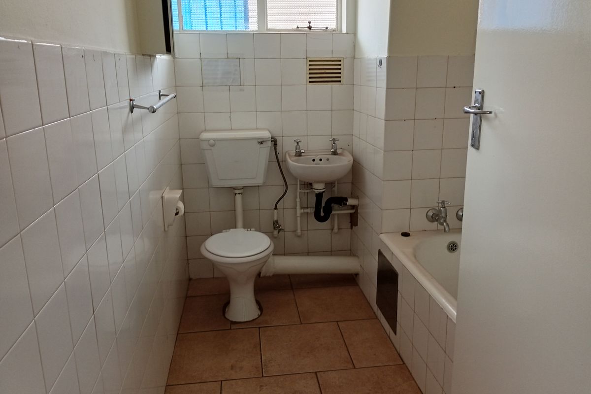 A compact, dated bathroom featuring a standard toilet, small wall-mounted basin, and a built-in bathtub with tiled walls and flooring.