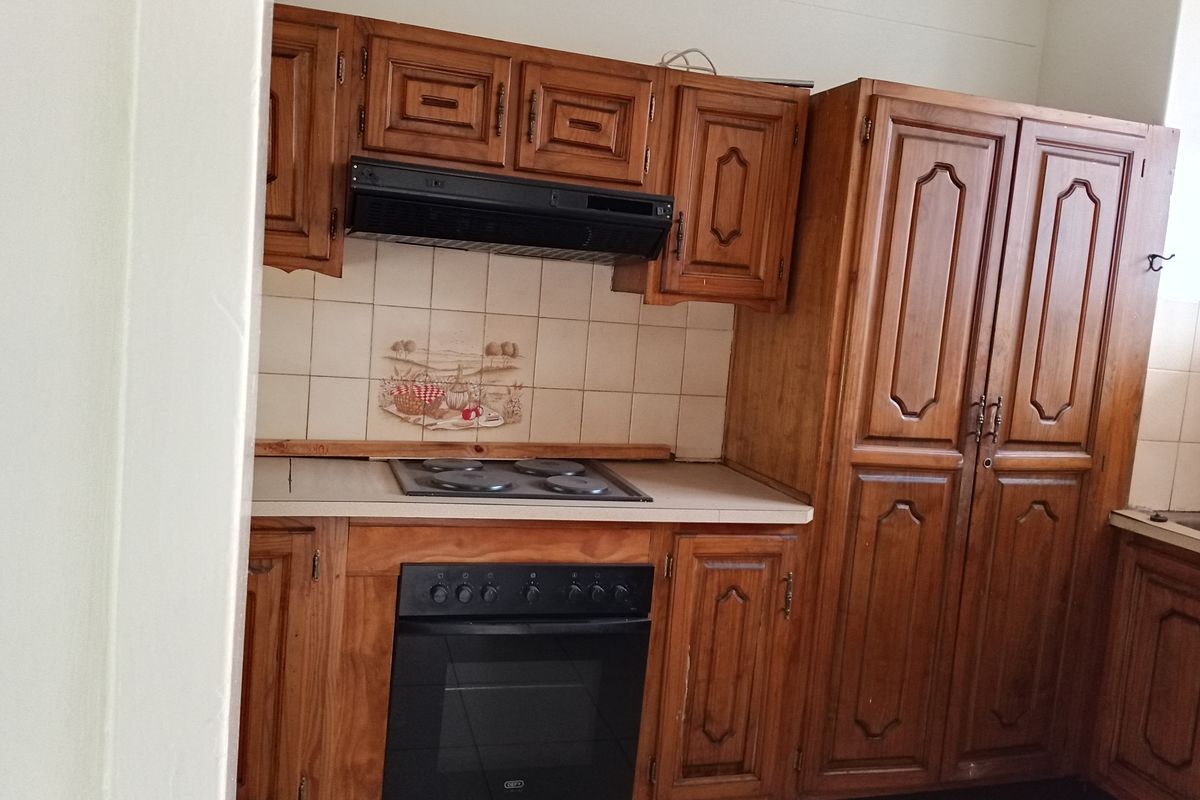 A functional kitchen featuring traditional wooden cabinetry, a built-in oven, electric hob, and an integrated extractor fan with tiled backsplash.