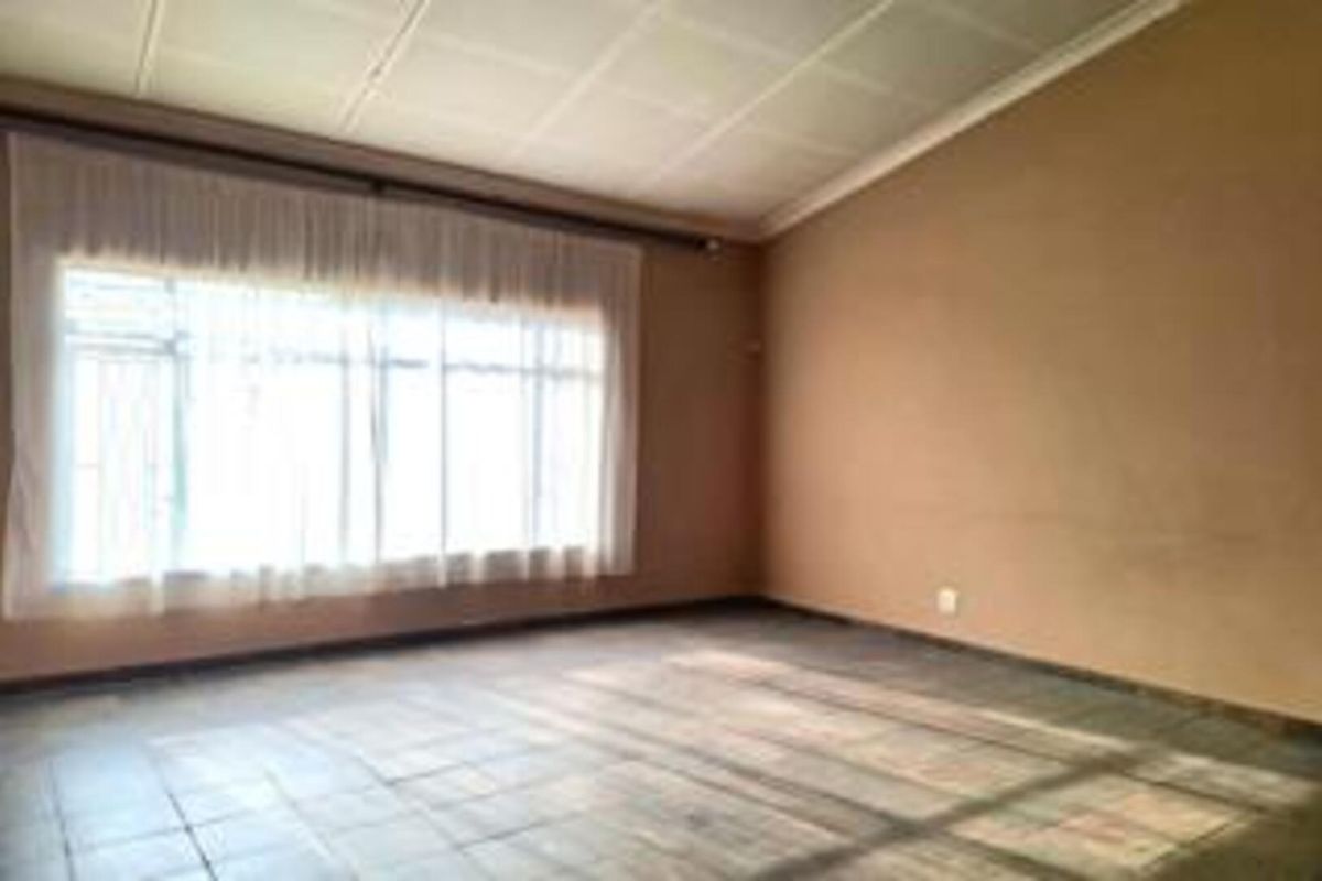 An empty living room featuring large windows with curtains, tiled flooring, and a suspended ceiling, offering a blank canvas for renovation.