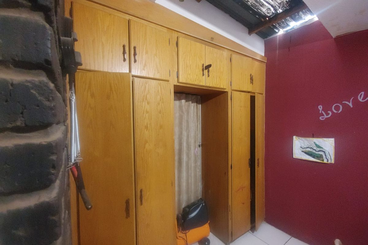 A bedroom featuring built-in wooden cabinetry with integrated storage and tiled flooring, showing signs of wear and ceiling damage.