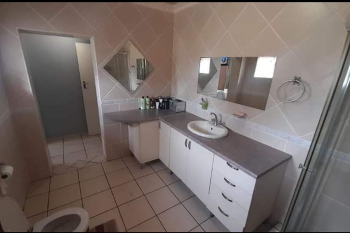 A functional bathroom featuring a built-in vanity with integrated basin, shower enclosure, and tiled walls and flooring.