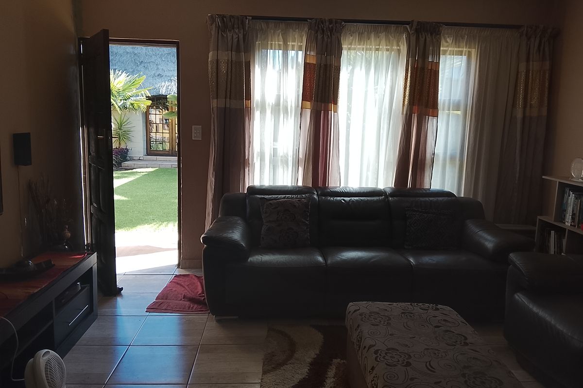 A living room featuring tiled flooring and large windows with curtains, providing direct access to an outdoor garden area.