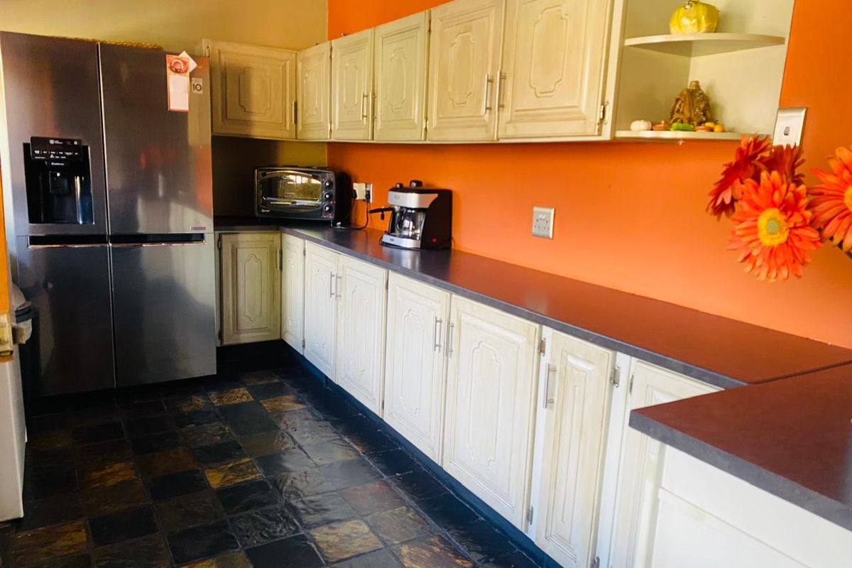 A functional kitchen featuring light-toned cabinetry, dark countertops, and slate-style floor tiling, set against a vibrant orange accent wall.