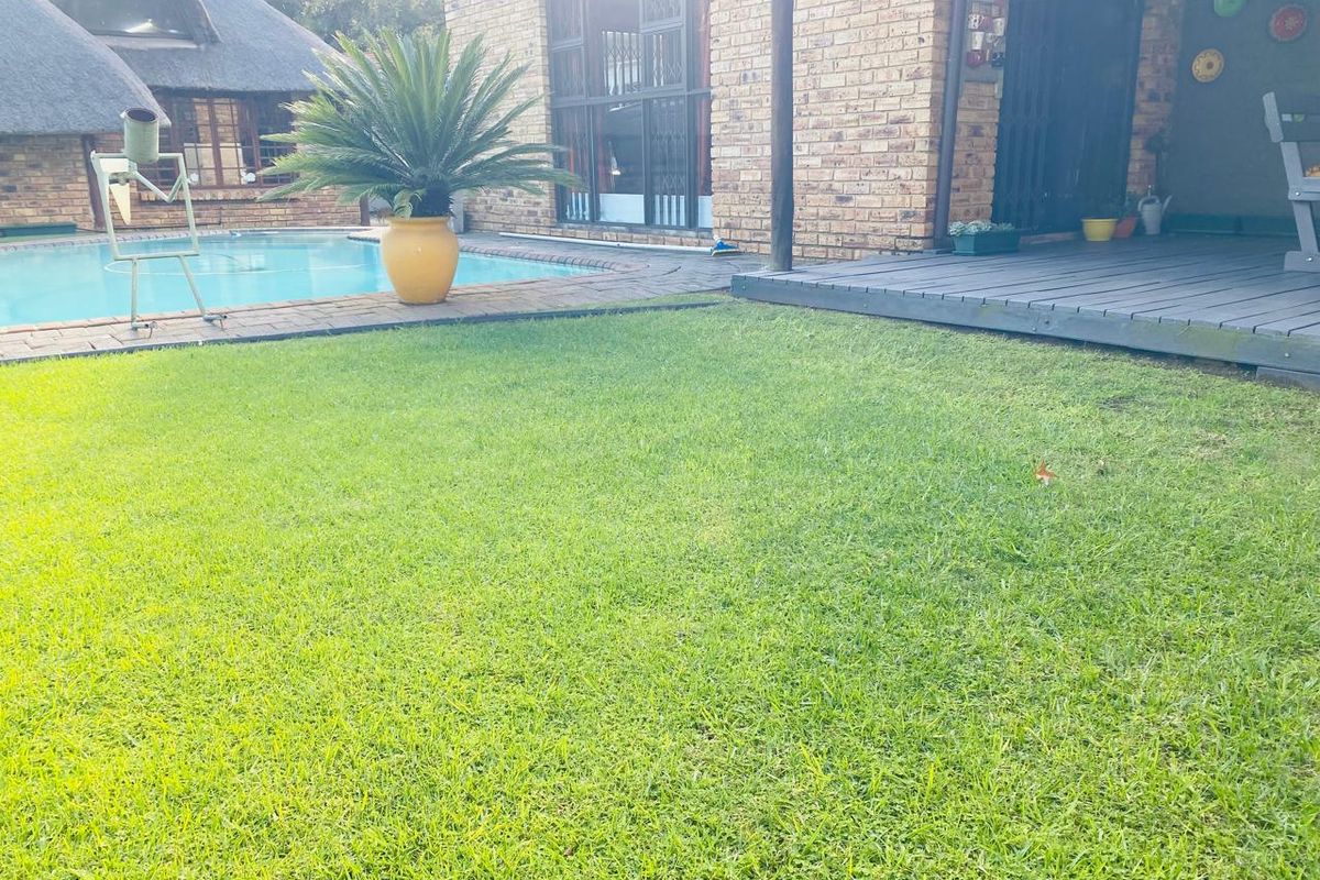 A well-maintained backyard featuring a swimming pool, a brick-faced exterior, and a raised wooden deck area.