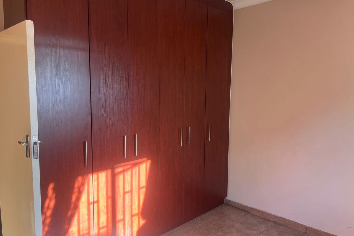 A bedroom featuring built-in wooden cupboards with modern handles and tiled flooring.