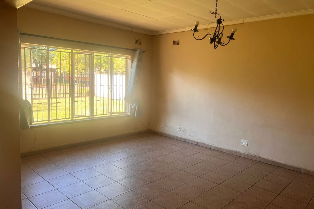 A spacious, empty living room featuring tiled flooring, large windows with security bars, and a central ceiling light fixture.