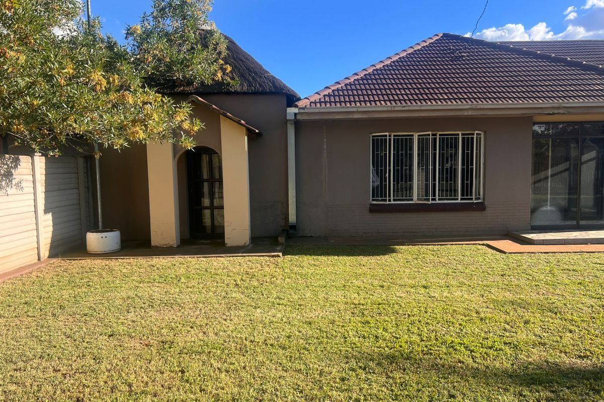 Rear view of the property featuring a thatched roof section, tiled roof, lawn area, and security bars on windows.