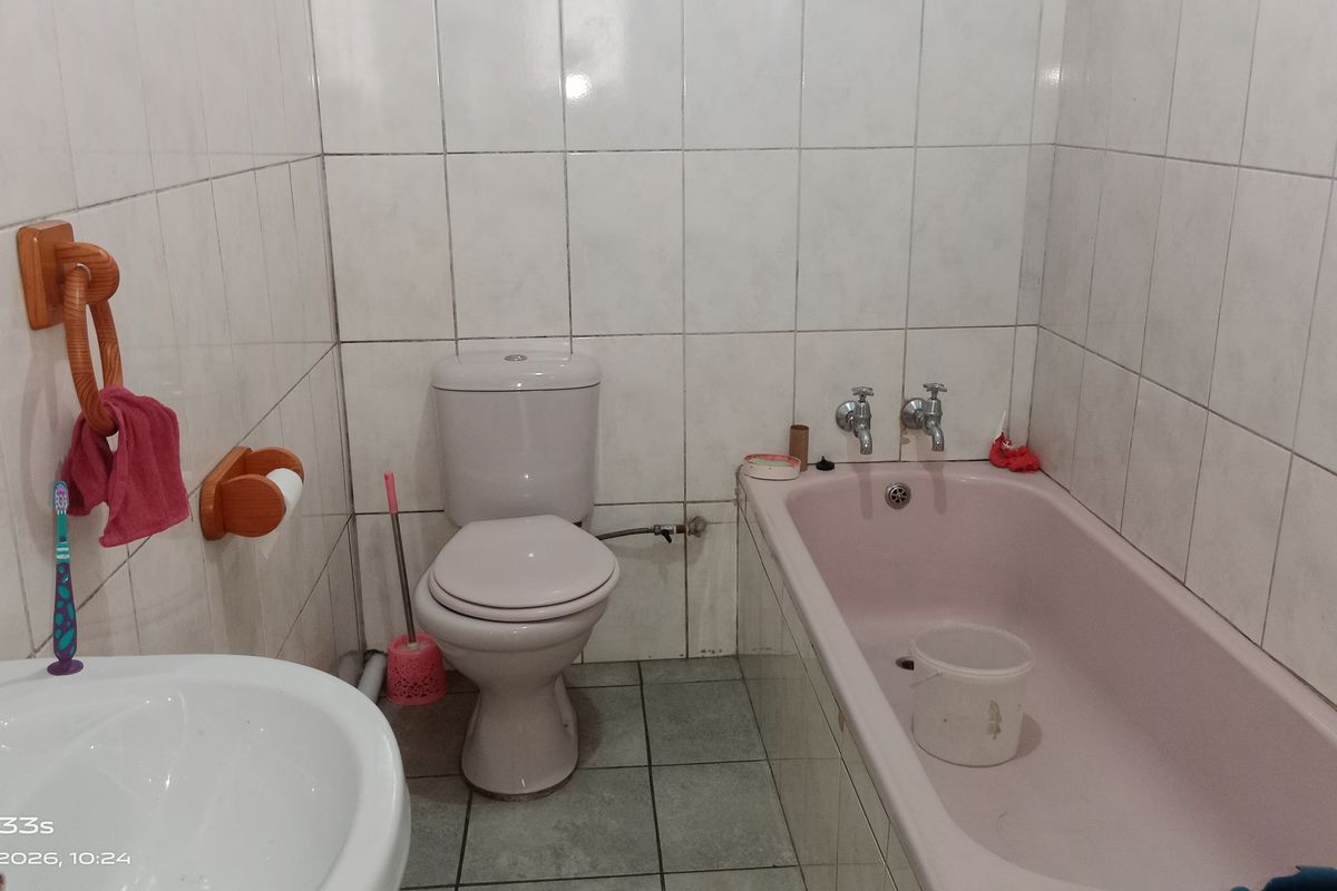A functional bathroom featuring a classic pink bathtub, white ceramic toilet, and pedestal basin with full-height wall tiling.