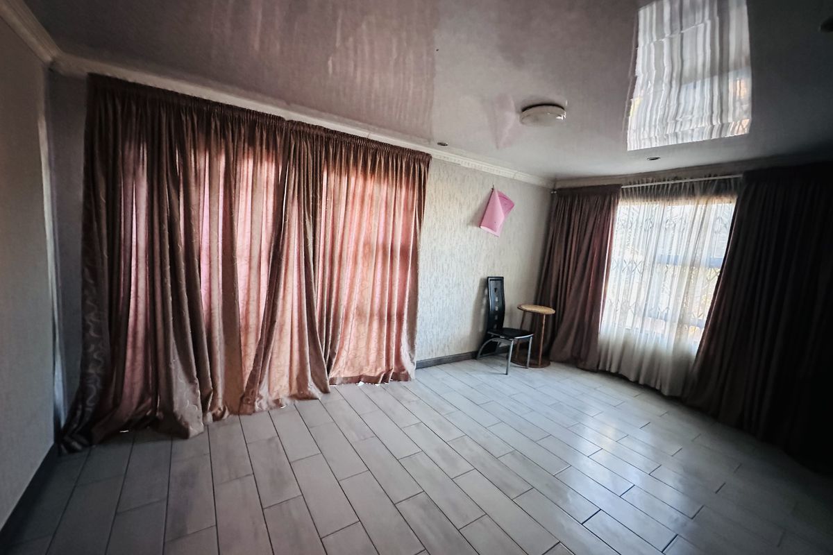 A spacious living room featuring tiled flooring, a glossy ceiling finish, and large windows dressed with floor-to-ceiling curtains.