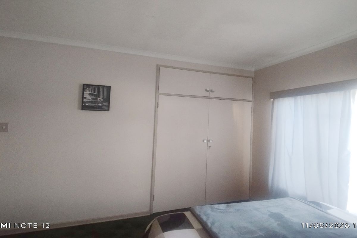 A bedroom featuring built-in cupboards and a window with natural light, providing a functional and neutral living space.