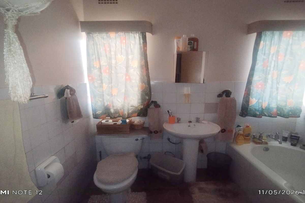 A dated bathroom featuring a pedestal sink, standard bathtub, and wall-mounted toilet, with tiled splashbacks and window treatments.