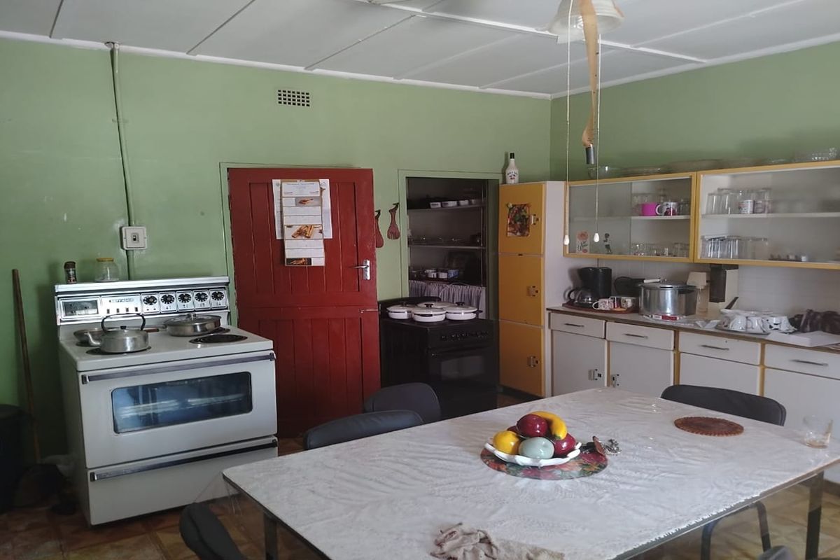 A dated kitchen featuring built-in cabinetry, a freestanding stove, and an adjacent scullery area, offering potential for modernization and renovation.