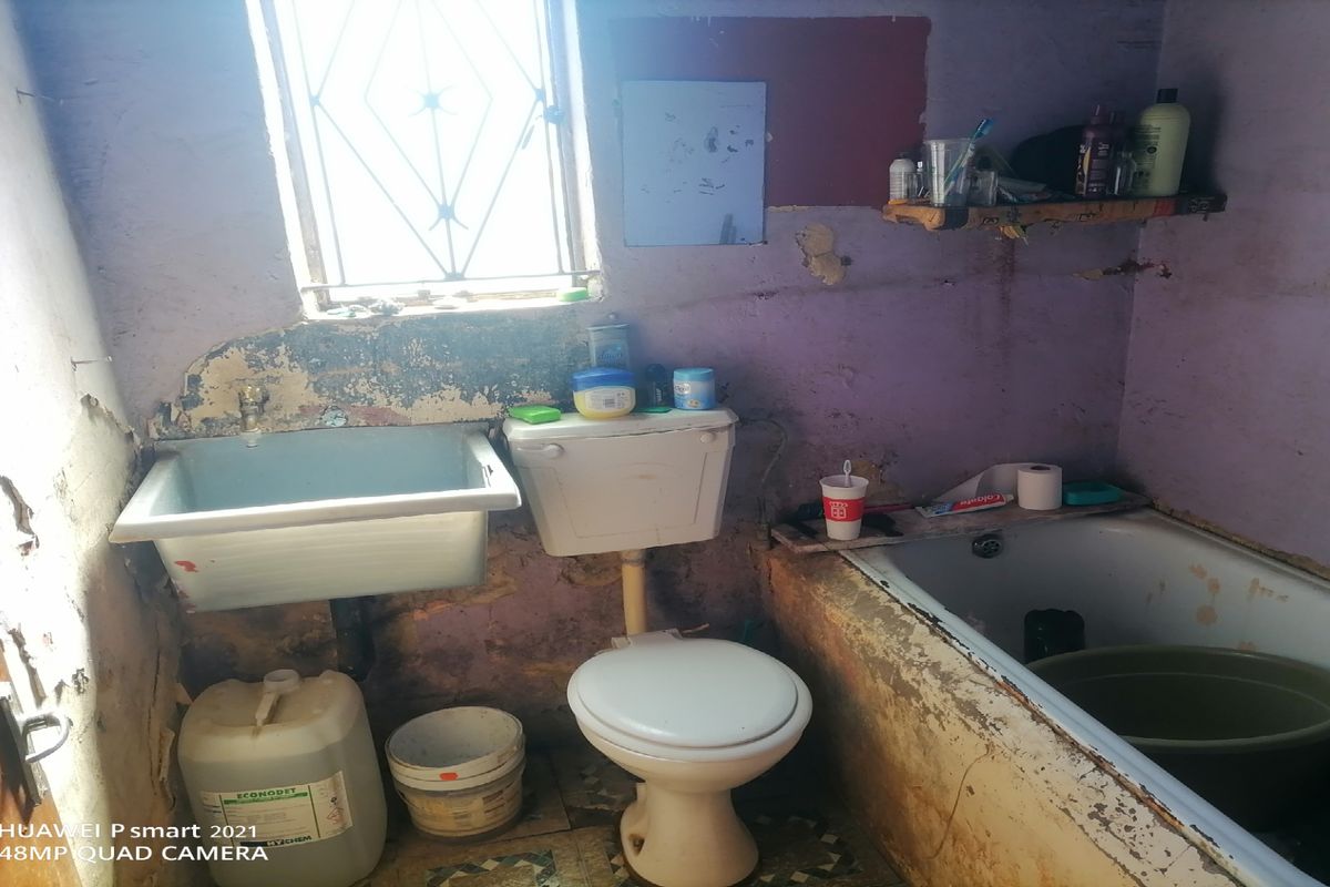 A bathroom featuring a standard bathtub, toilet, and wall-mounted basin, requiring significant renovation and repair to the wall finishes and fixtures.