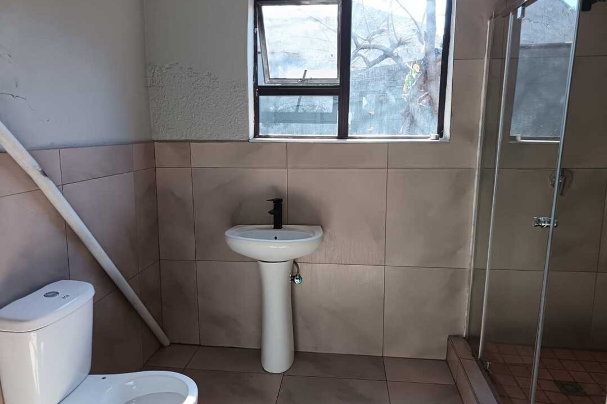 A functional bathroom featuring a pedestal basin, toilet, and glass-enclosed shower, requiring minor cosmetic repairs and finishing touches to the wall surfaces.