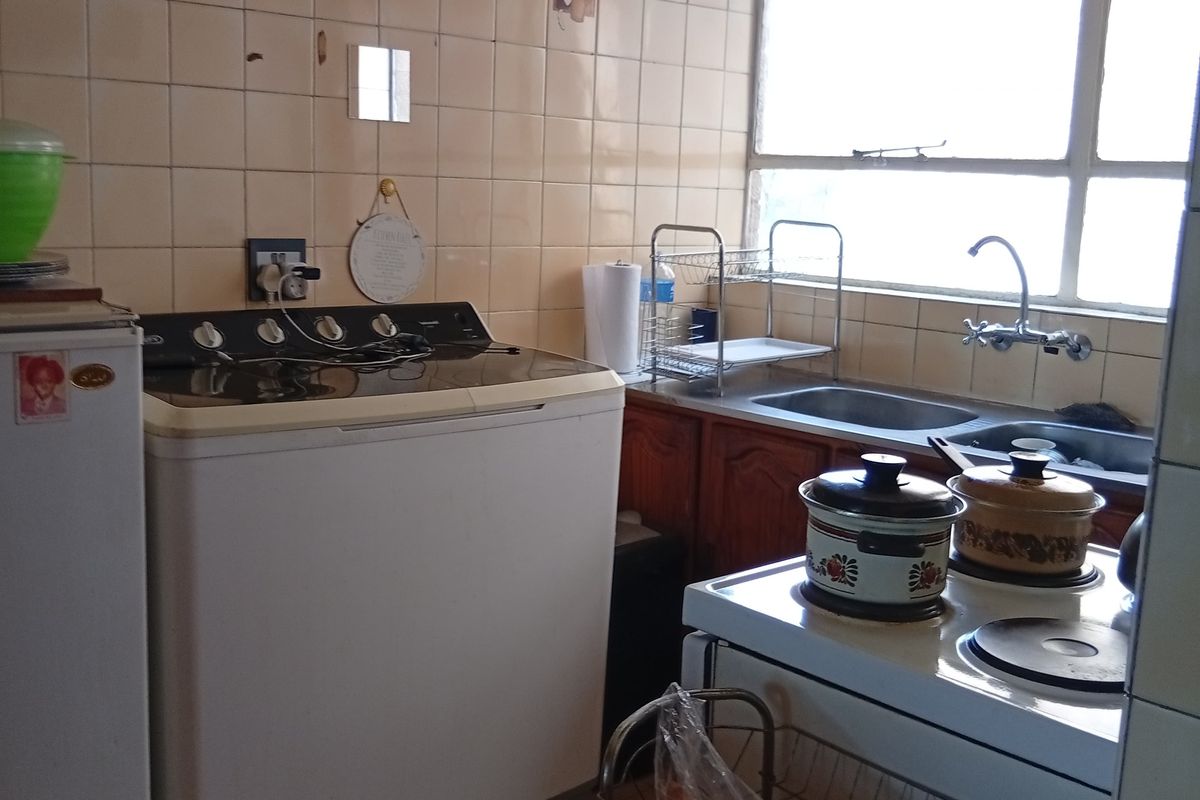 A functional kitchen and laundry area featuring tiled walls, double sink, and built-in cabinetry, requiring cosmetic updates to modernize the space.