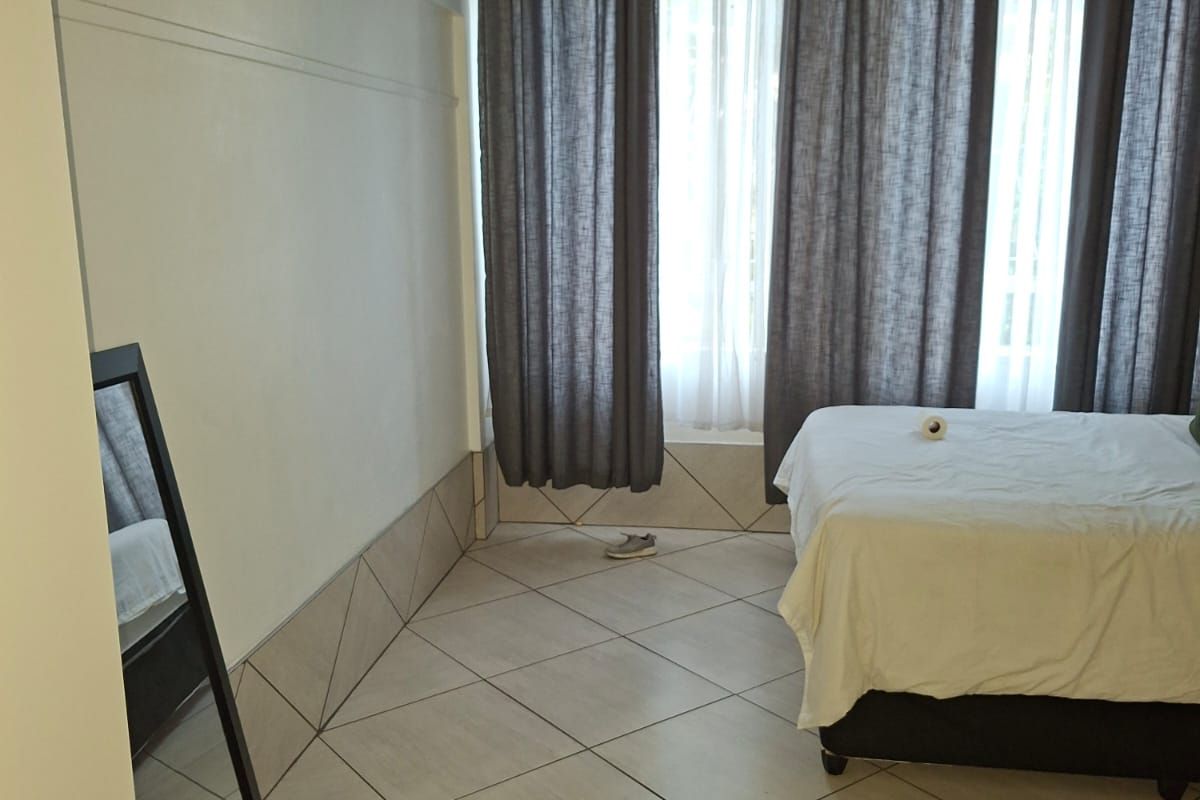 A bedroom featuring large format floor tiles and a window with curtain tracks.