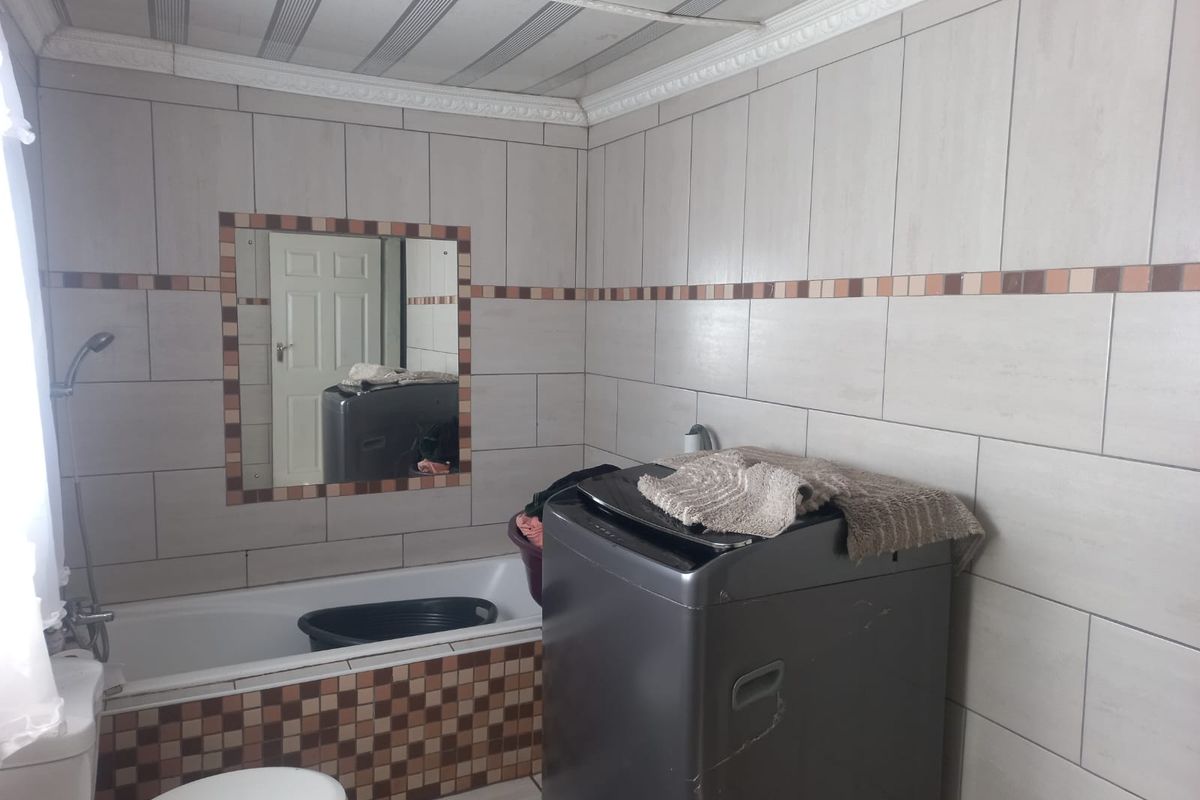 A functional bathroom featuring a bathtub, toilet, and wall-mounted shower head, finished with neutral wall tiles and a decorative mosaic border.