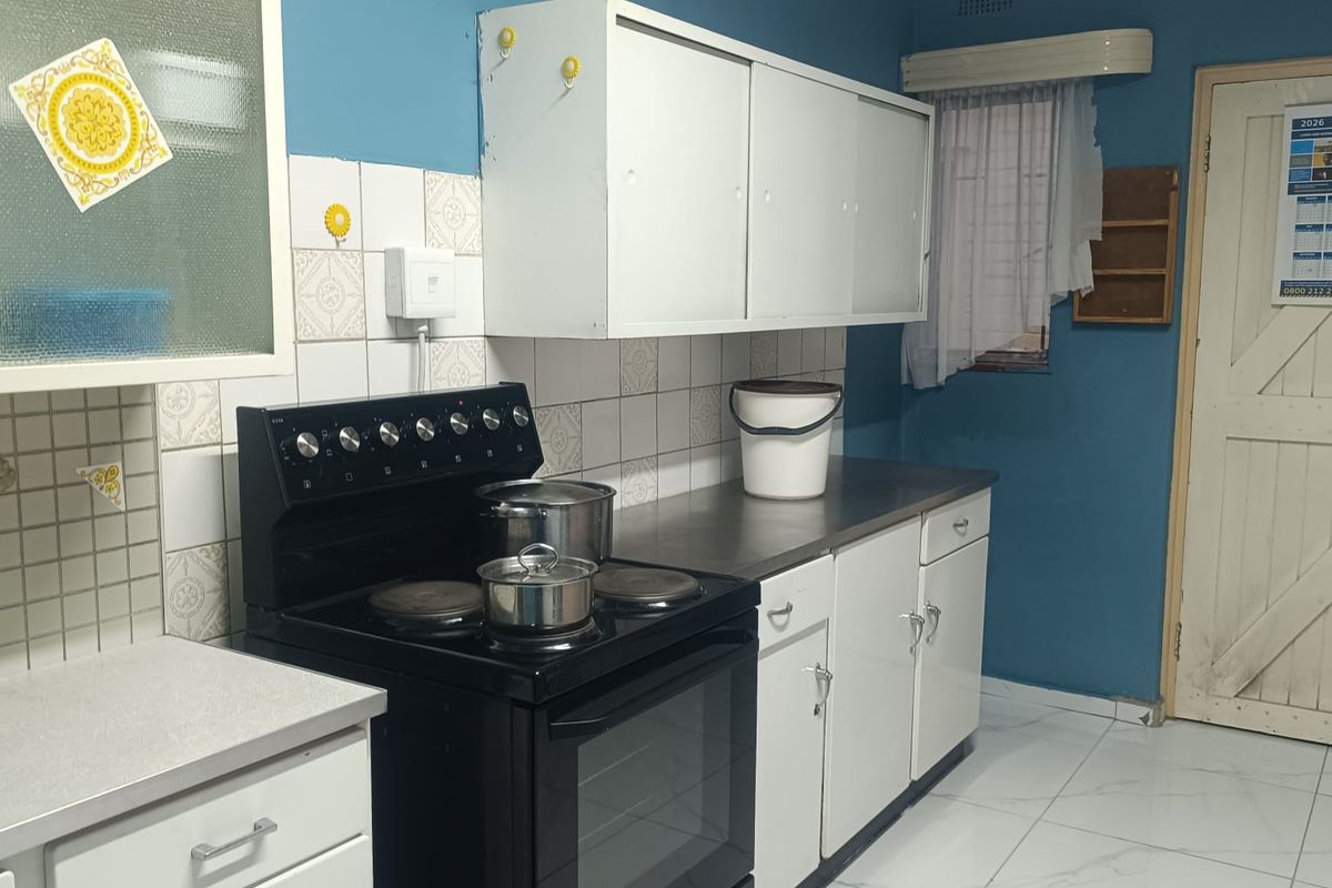 A functional kitchen featuring white cabinetry, tiled splashbacks, and a freestanding black stove, finished with modern floor tiles.