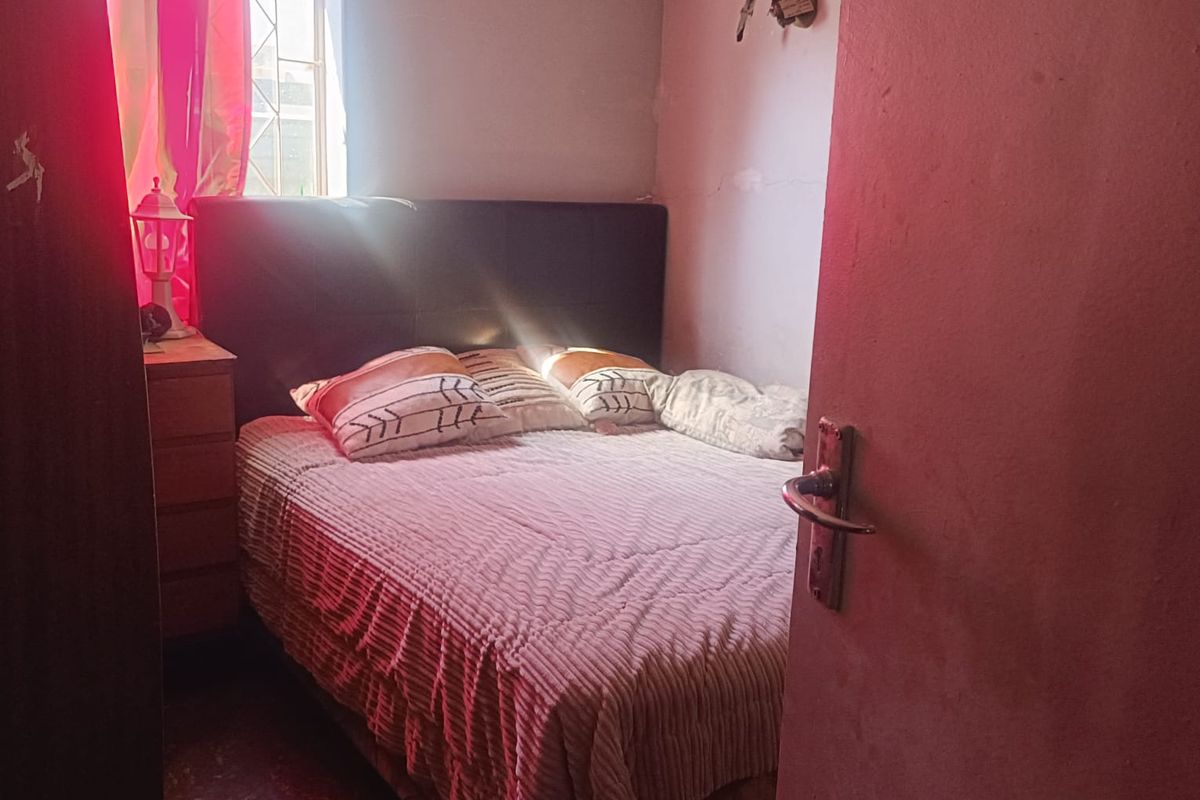 A compact bedroom featuring a window with natural light, tiled flooring, and a built-in wall shelf.