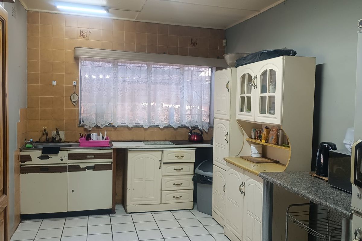 A dated kitchen featuring traditional cabinetry, tiled backsplash, and tiled flooring, offering a functional layout with potential for modernization and cosmetic updates.