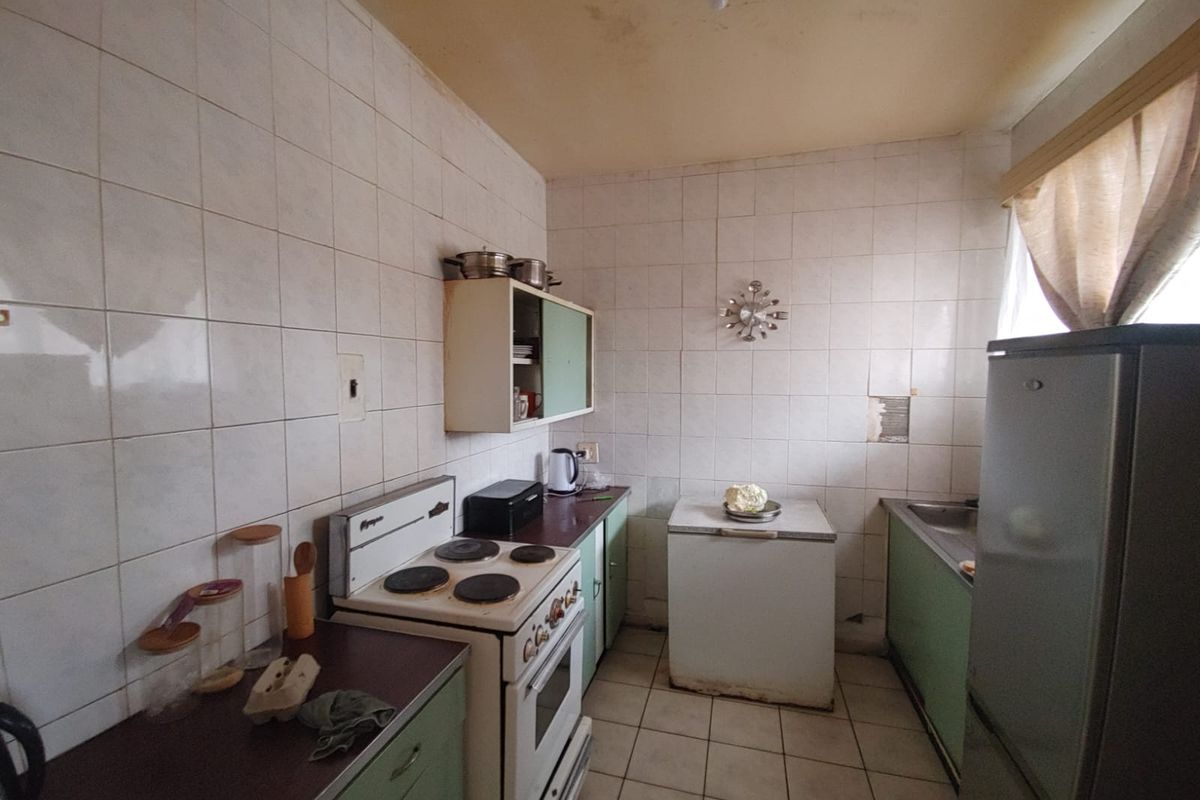 A dated kitchen featuring original cabinetry, tiled walls, and floor, requiring modernization to improve functionality and aesthetic appeal.