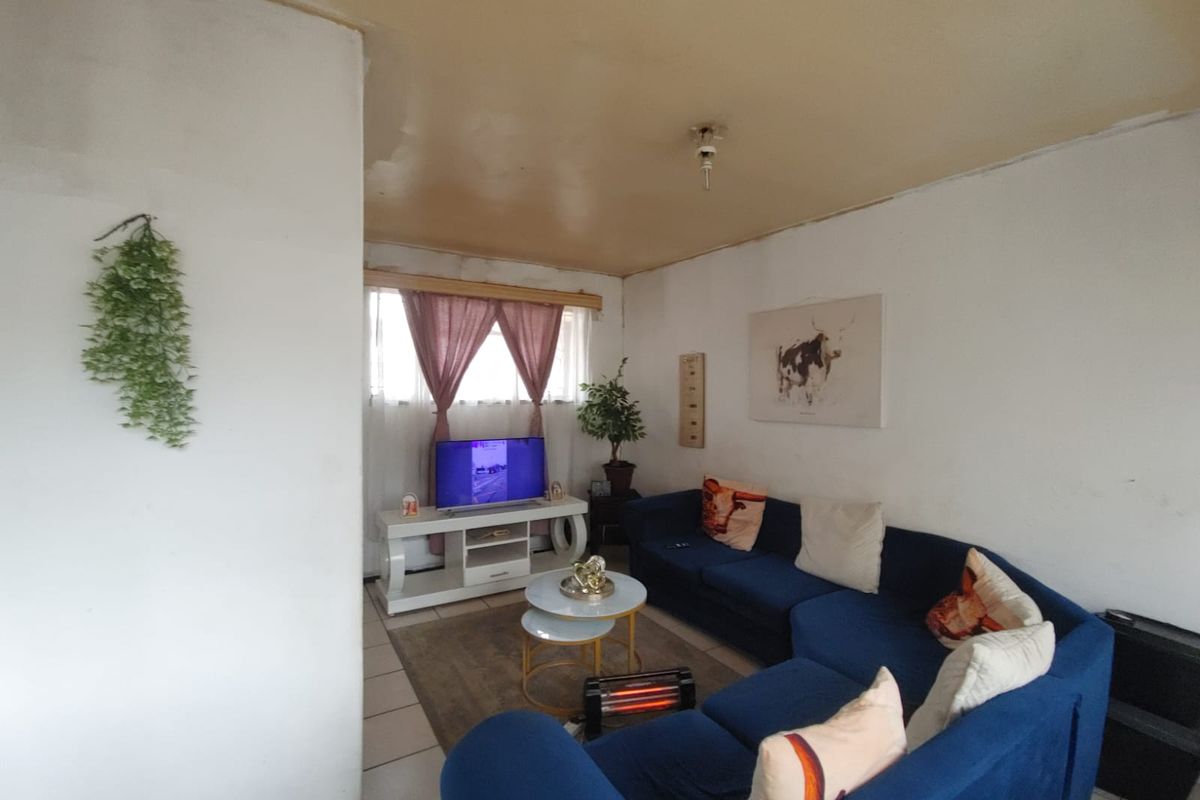 A living room featuring tiled flooring and a window with natural light, requiring cosmetic updates to the ceiling and wall finishes.