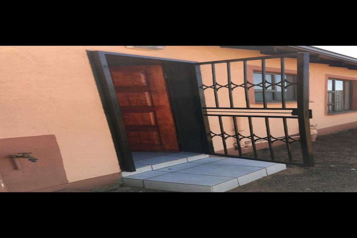 Exterior view of a side entrance featuring a security gate, tiled step, and wooden door, with an external water tap visible on the wall.