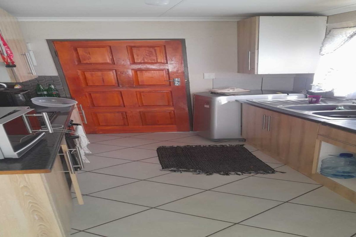 A functional kitchen featuring wood-look cabinetry, tiled flooring, a double sink, and direct access to an exterior wooden door.