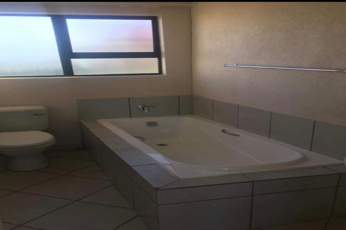 A functional bathroom featuring a built-in bathtub with tiled surround, a standard toilet, and a wall-mounted towel rail.
