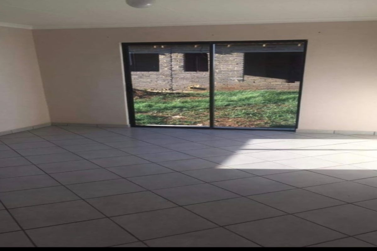 An empty living room featuring neutral tiled flooring and a large sliding glass door providing access to the rear exterior.