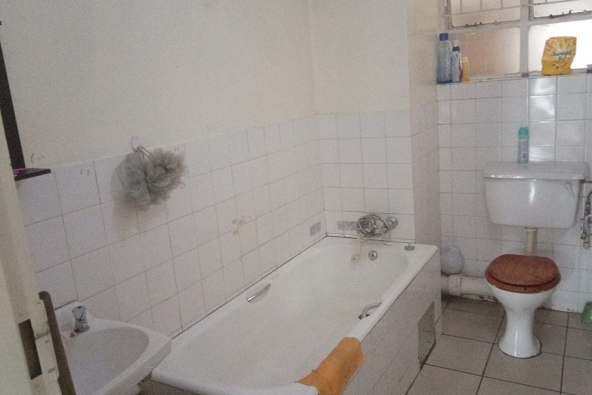 A functional bathroom featuring a standard bathtub, pedestal basin, and toilet with tiled walls and flooring.
