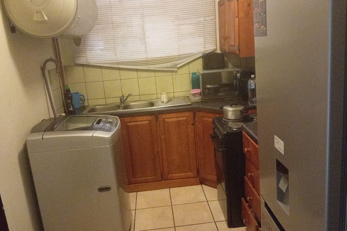 A compact kitchen featuring wooden cabinetry, tiled splashbacks, a double sink, and space for a washing machine and freestanding stove.