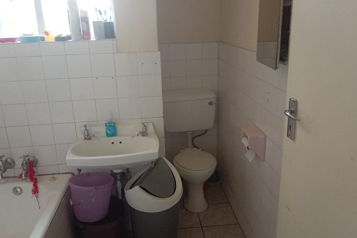 A dated bathroom featuring a standard bathtub, wall-mounted basin, and toilet with white wall tiling.