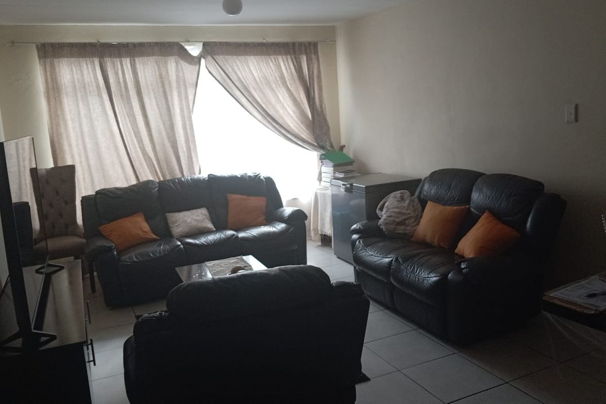 A living room area featuring tiled flooring and large windows with curtains, providing a functional and comfortable space for relaxation.